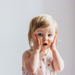 Surprised shocked child toddler girl with hands on her cheeks isolated on light background